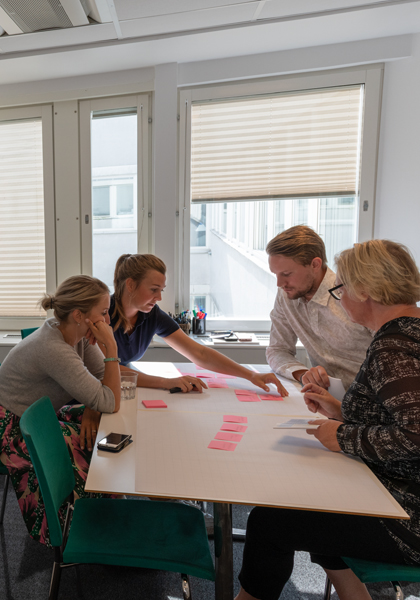 4 personer samlade runt bord under utbildning & kurs och kollar på rosa post-it lappar