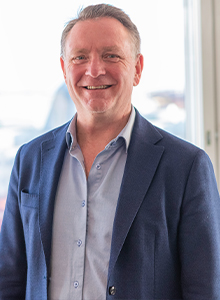 Man står med kavaj leende mot kameran